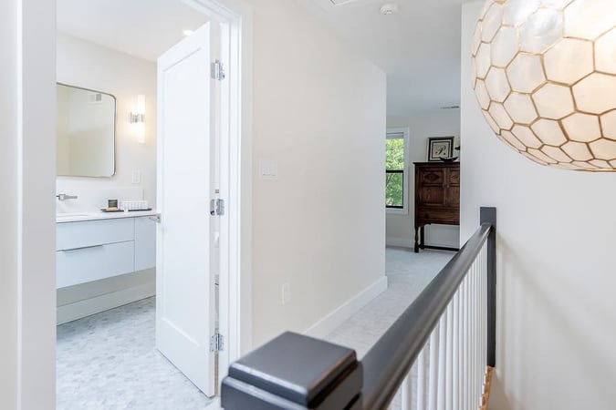Long hallway with cream walls leading to white transitional bathroom by Bellweather Design-Build in Philadelphia