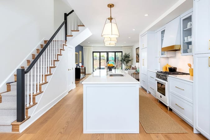 Philadelphia transitional white kitchen with staircase to left and island in middle by Bellweather Design-Build